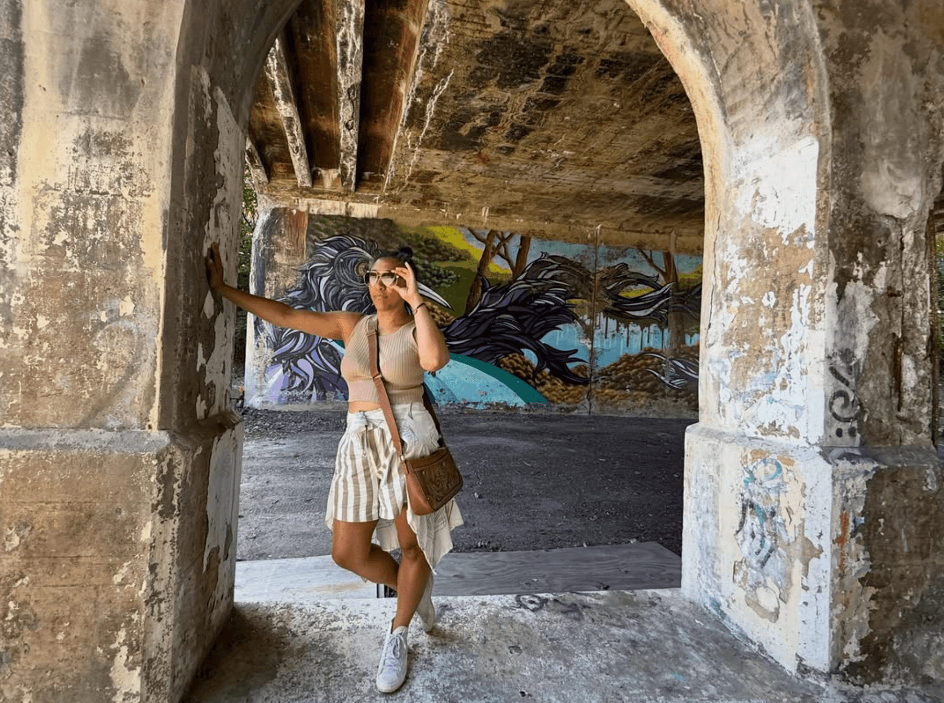 Autumn Hicks standing beneath a textured concrete archway with neighborhood mural art behind her